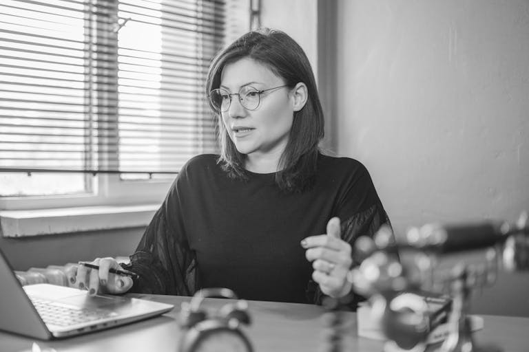 Black and white portrait of a woman using a laptop at a desk, engaging in a video call.